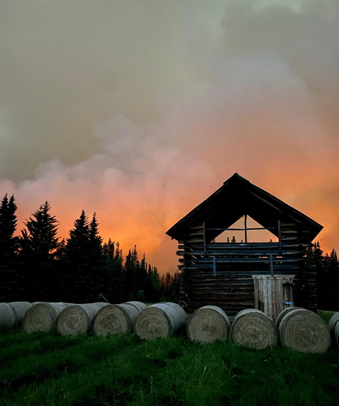 Silhouette of barn-like structure and hay bales backed by an orange, smoky sky from an approaching wildfire
