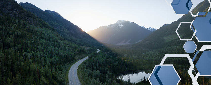 image of remote road in BC, between a lake and a tree-covered hill, with mountains in the backgrund