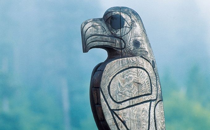 Indigenous carved eagle totem set against misty forest background. Indigenous carved eagle totem set against misty forest background.
