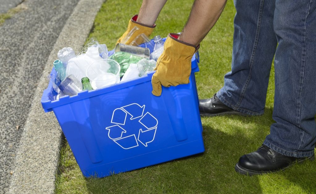 Person placing plastic bottles and cans into a blue recycling bin on grass. Person placing plastic bottles and cans into a blue recycling bin on grass.