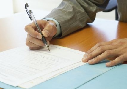 Person signing official documents on a wooden desk with blue folders. Person signing official documents on a wooden desk with blue folders.