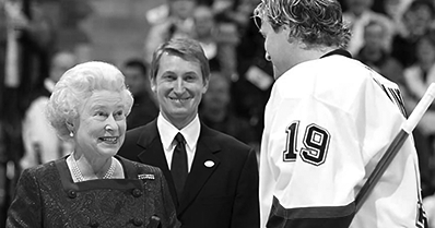 Queen Elizabeth II at a hockey game smiling at Vancouver Canucks player, Markus Naslund (#19) while Wayne Gretzky looks on