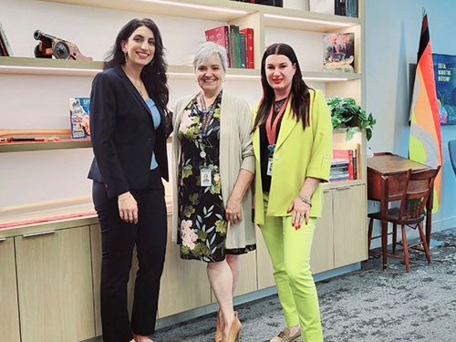 Three people stand in front of a bookcase.