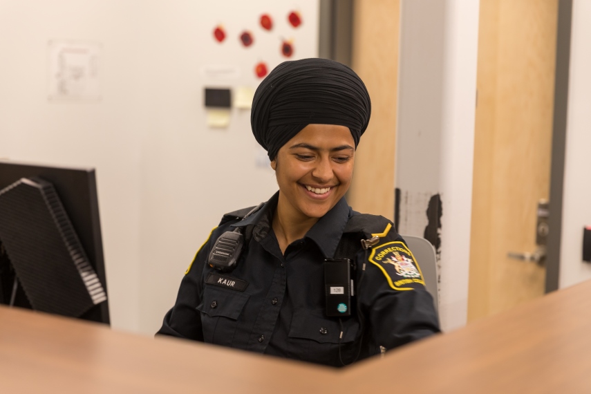 A bc correctional officer sitting at a reception desk smiling A bc correctional officer sitting at a reception desk smiling
