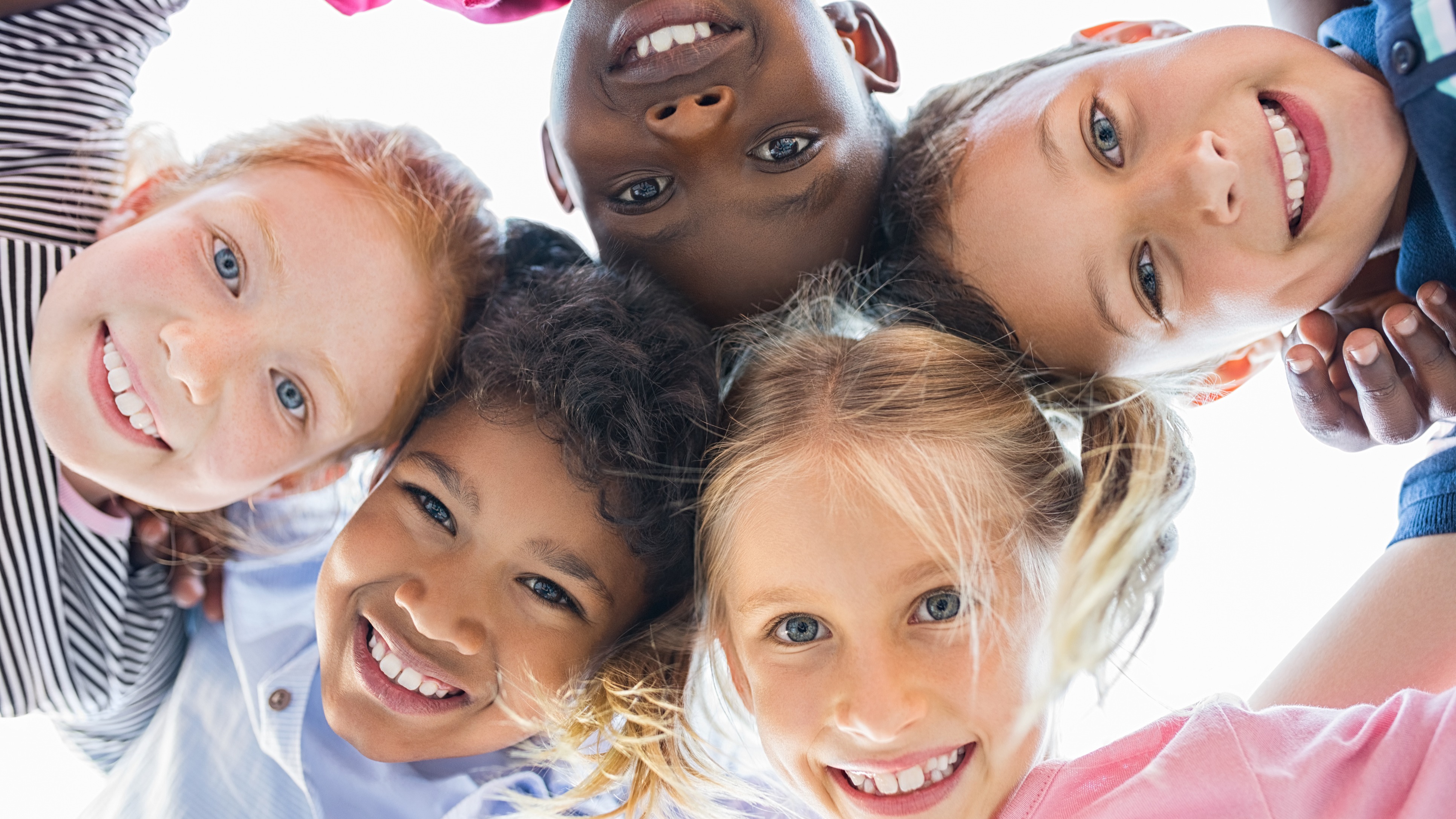 A group of children in a circle with arms around each other, smiling at the camera.
