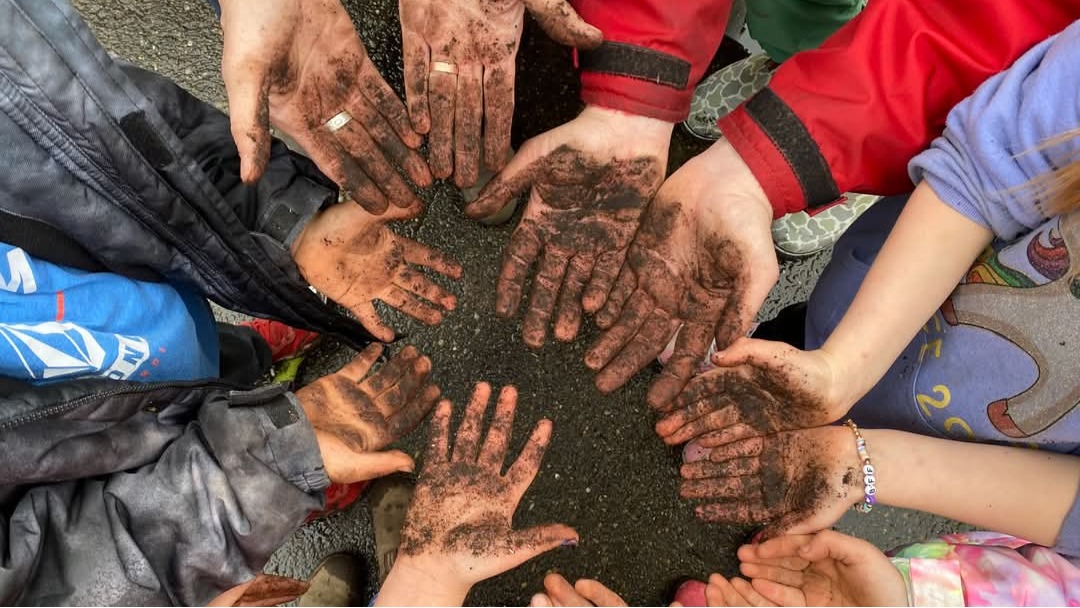 A circle of children's hands, covered in sand