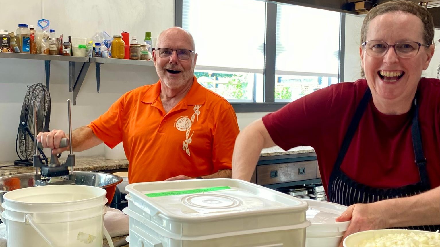 Two volunteers preparing food in a commercial kitchen.