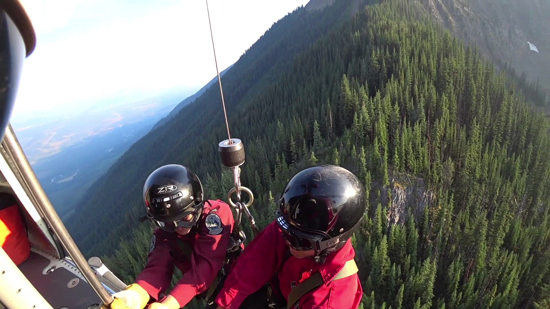 two members are lowered from an aircraft above a forest